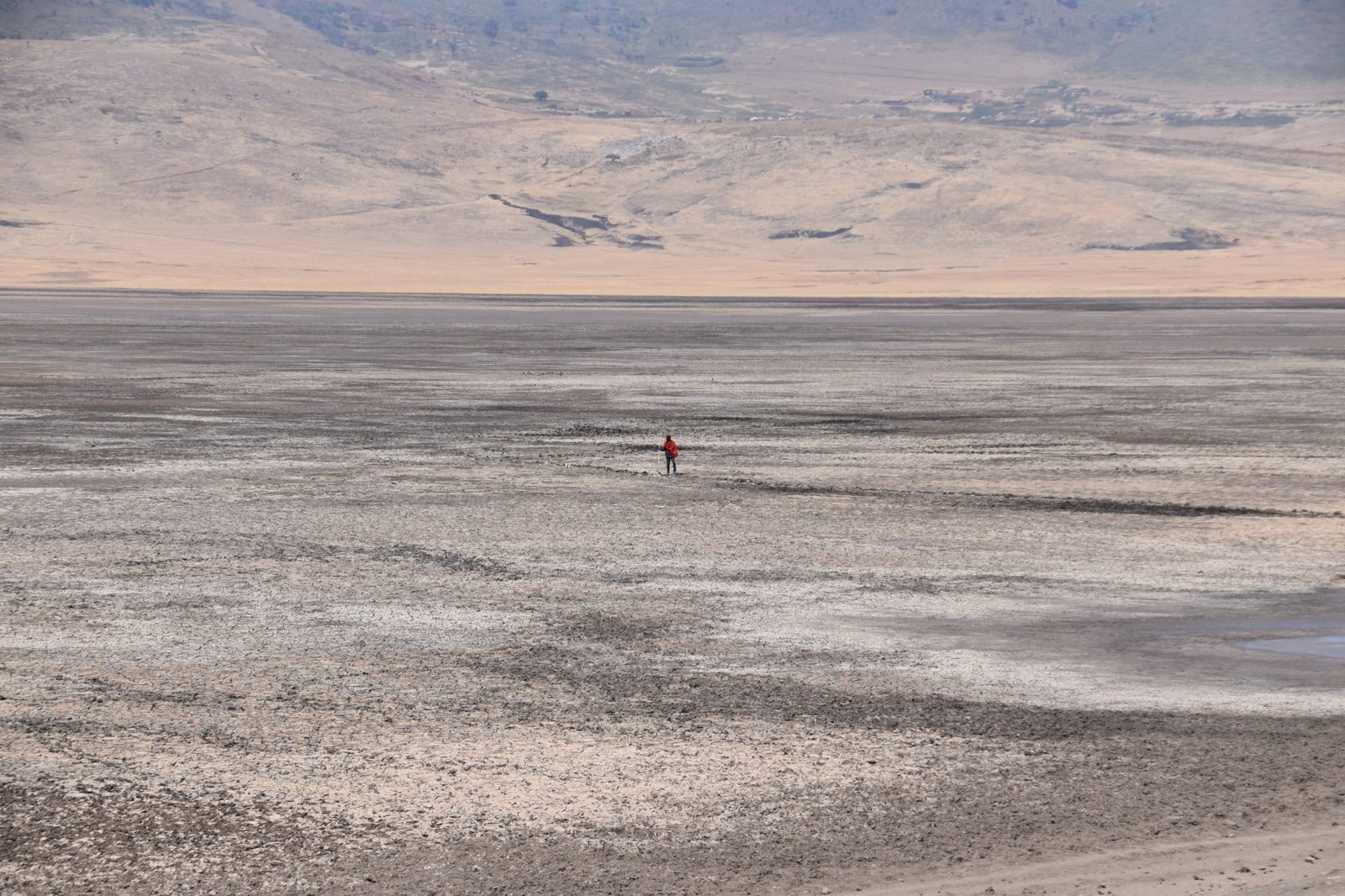 Lone figure in red crossing a vast dry plain