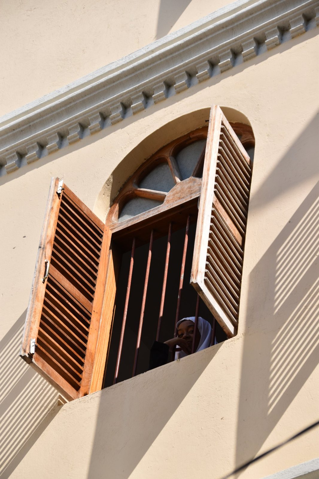 Girl looking out of an arched window with wooden shutters