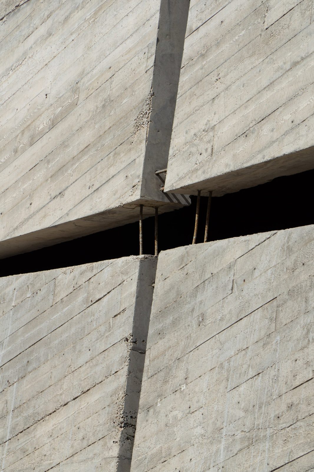 Board-marked concrete walls split by a dark gap with rusted rebar