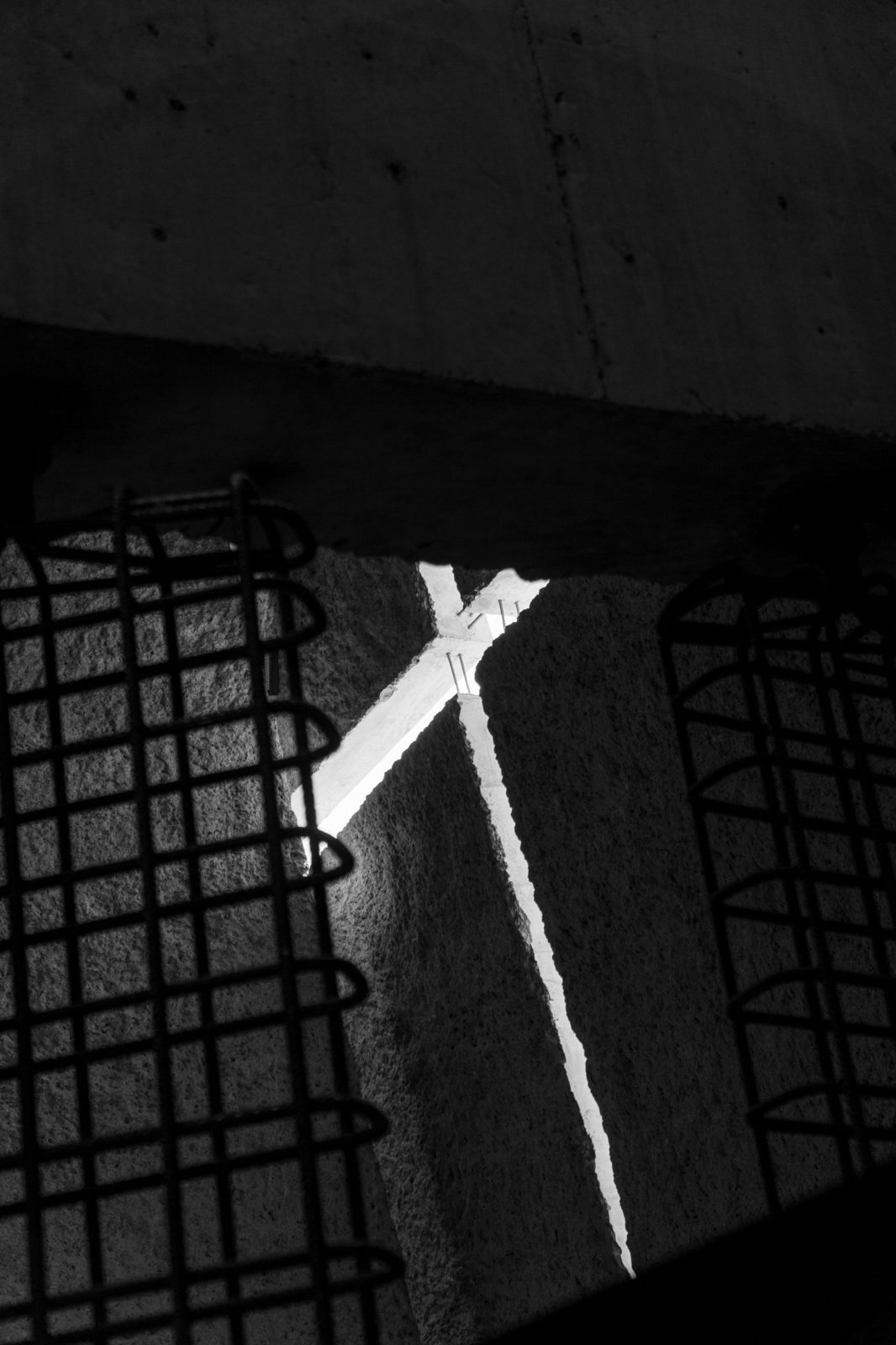 Shaft of light between rough concrete walls and rebar cages, black and white