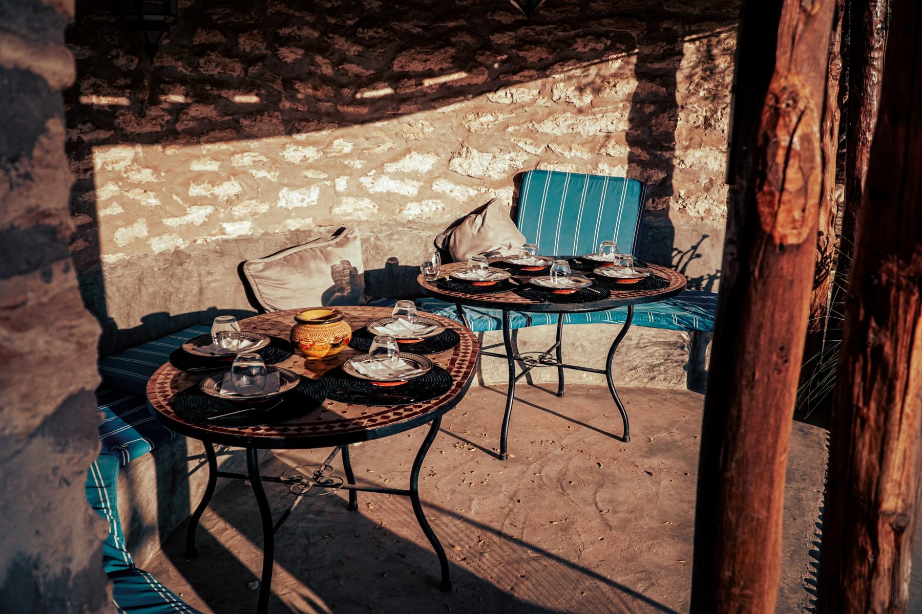 Mosaic tables set under a stone wall striped with sun and shadow